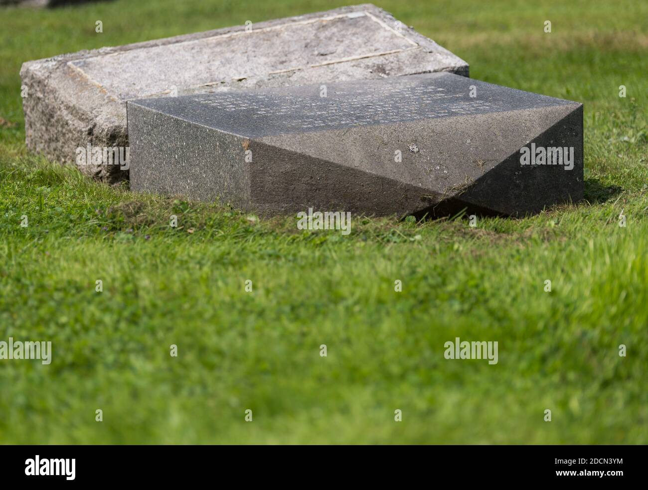 Broken grave marker. It has fallen over and is lying on the ground. Stock Photo