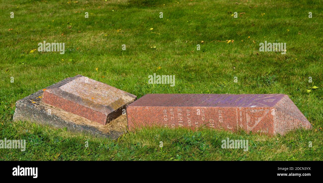 A broken grave marker. It is made from red granite, and has fallen over and is resting in the grass. There is room for text above. Stock Photo