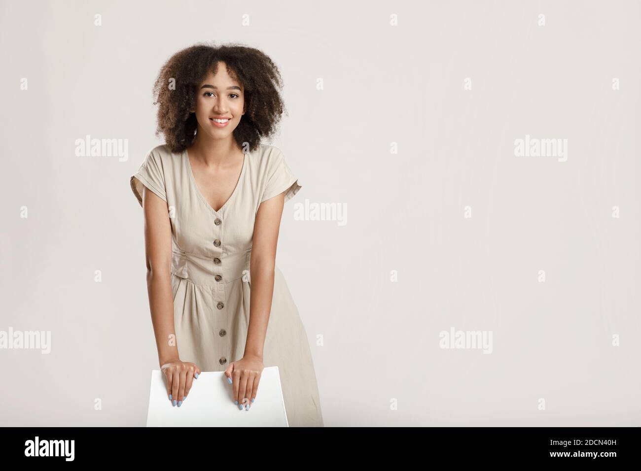 Portrait of cheerful curly african american young woman leaning on chair looking at camera and smiling Stock Photo