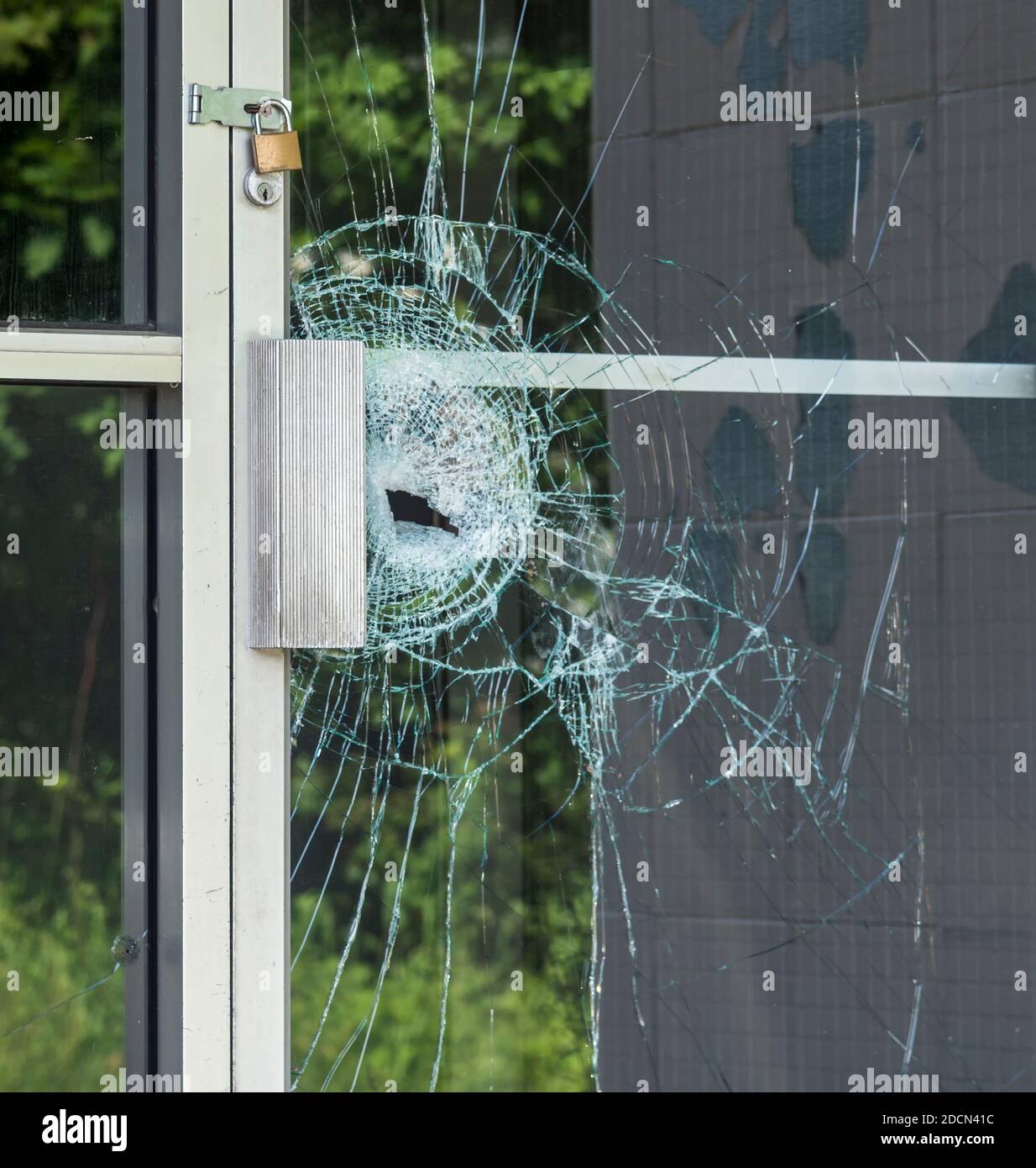 A broken glass window in an aluminum frame door. Door is padlocked. Stock Photo