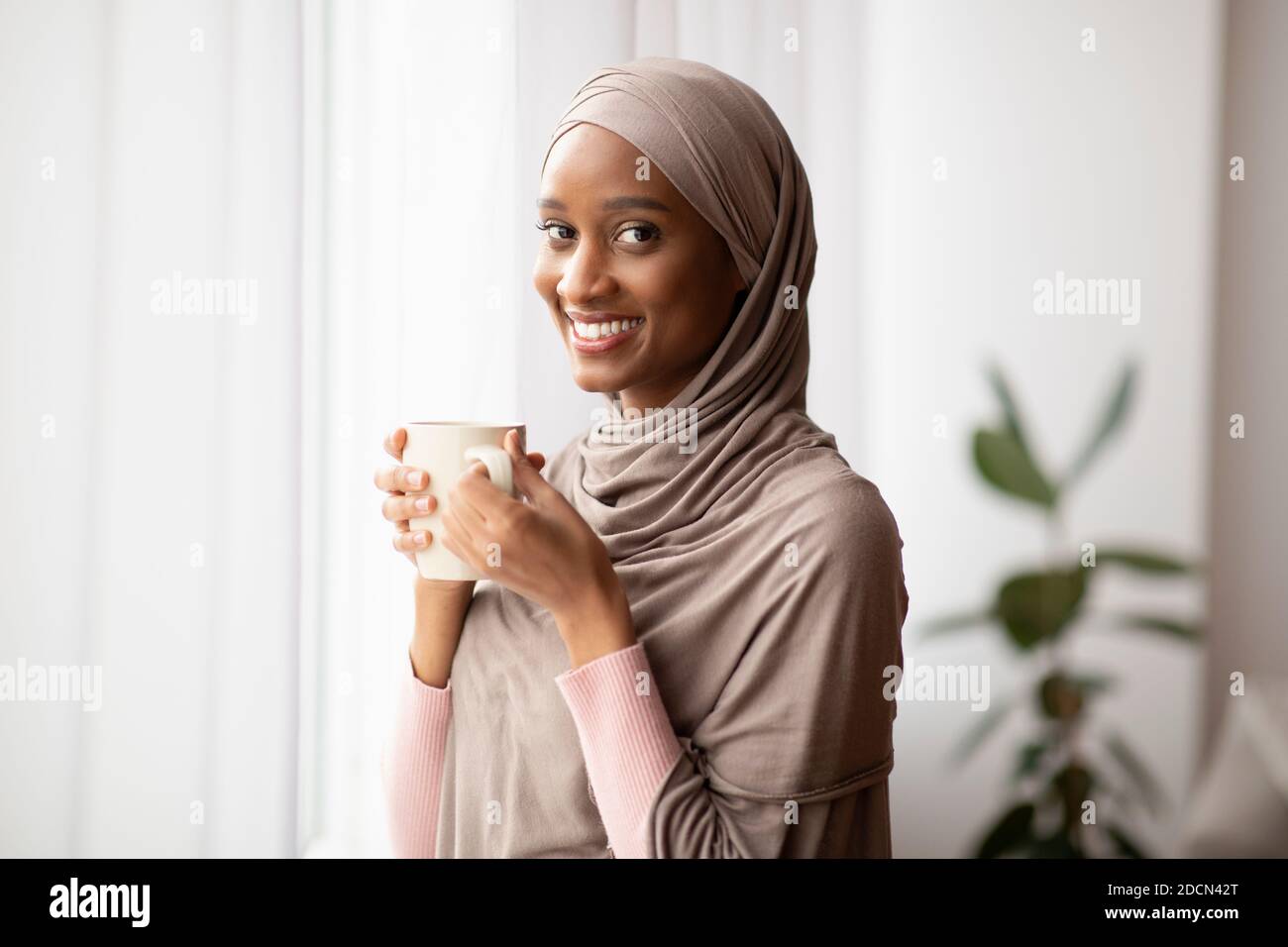 Black Muslim woman in traditional hijab drinking hot aromatic coffee ...