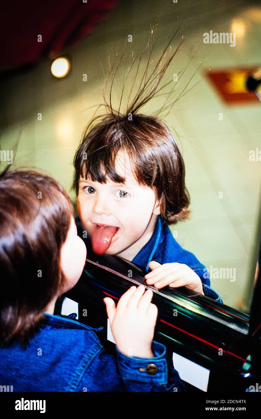 A young girl sticking her tongue out in a mirror with her hair standing