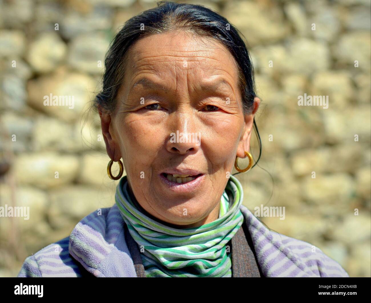 Elderly Nepali Sherpa woman with traditional golden earrings poses for the camera on Everest Base Camp Trek. Stock Photo