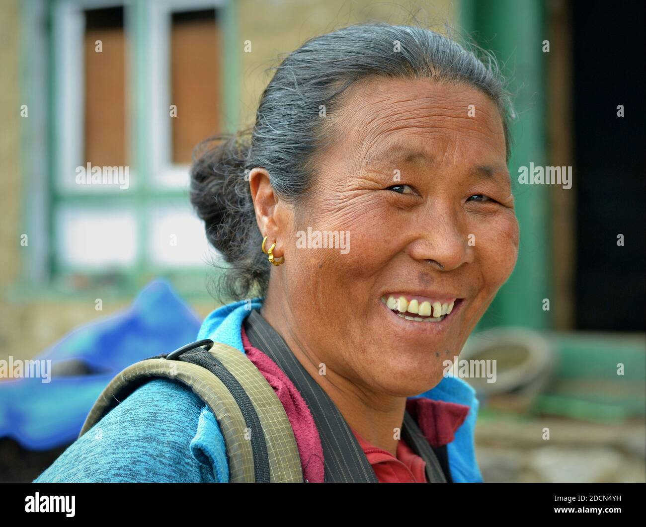 Happy elderly Nepali woman of Tibetan origin smiles for the camera in front of her village home. Stock Photo