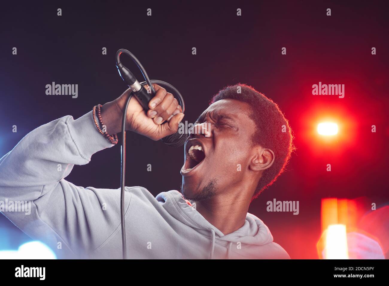 Portrait of young African-American man singing to microphone passionately while standing on stage in lights, copy space Stock Photo