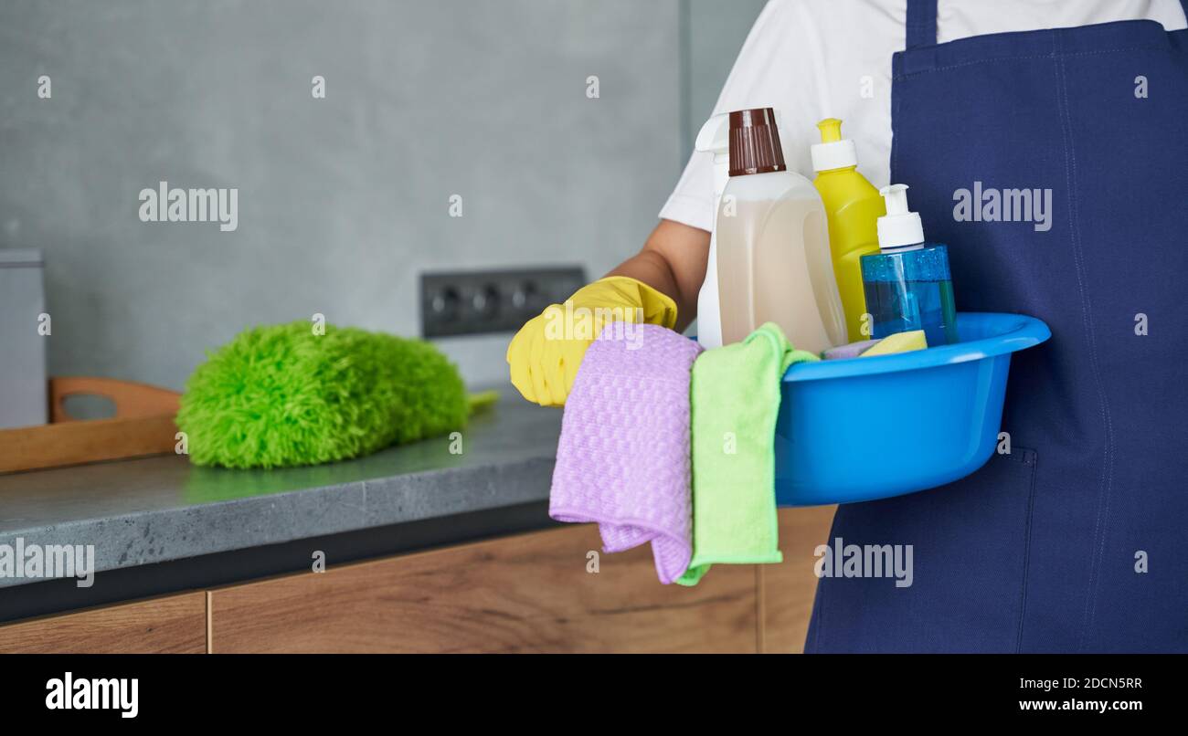 Close up of cleaning lady holding container full of cleaning products and equipment while standing in the modern kitchen. Housework and housekeeping, cleaning service concept Stock Photo