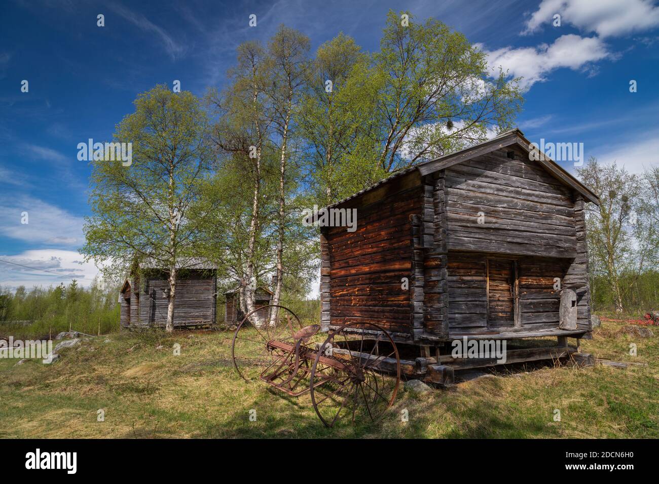 Old wooden Sami storage sheds with a historic hay rake on a sunny summer morning in Tjåmotis, Lapland, Sweden Stock Photo