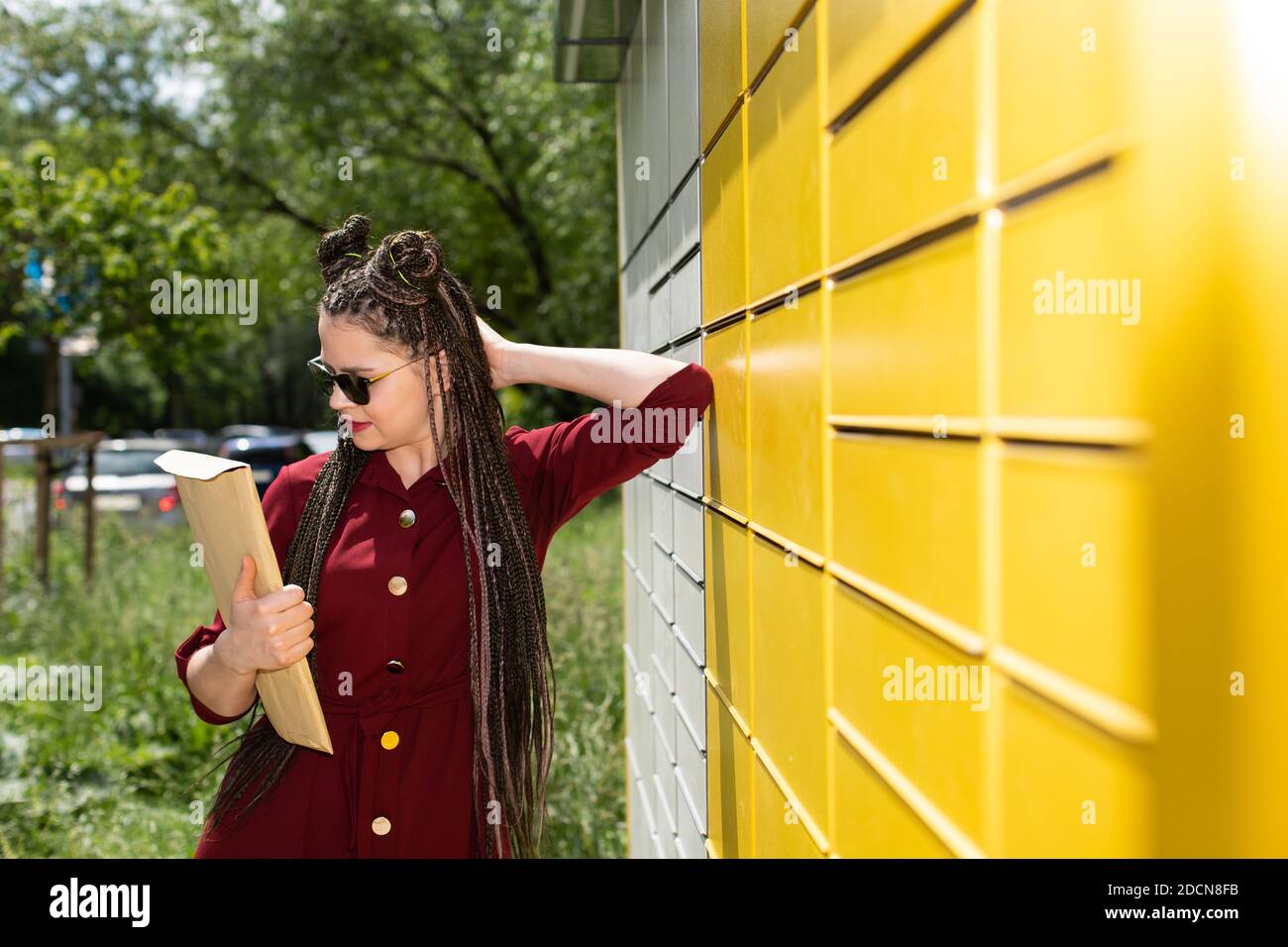 On an unusually sunny day in the summer, the girl went to collect a package from the neighborhood parcel warehouse and stands reading from whom she received it. Stock Photo
