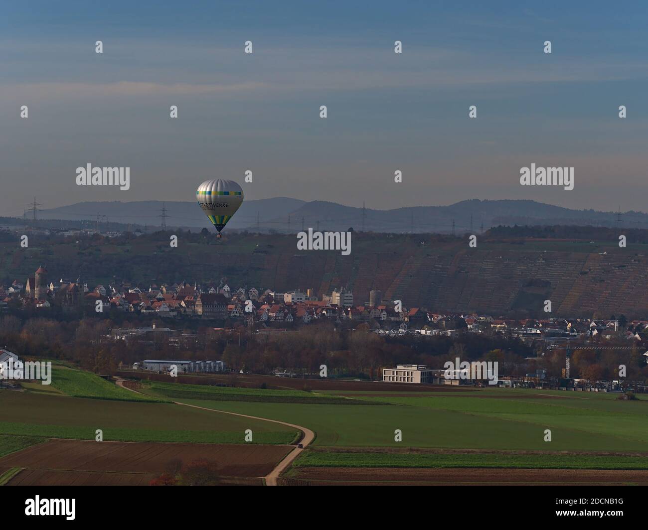 Hot air balloon branded by utility company Stadtwerke Stuttgart flying at low altitude above agricultural fields in autumn with town Besigheim. Stock Photo