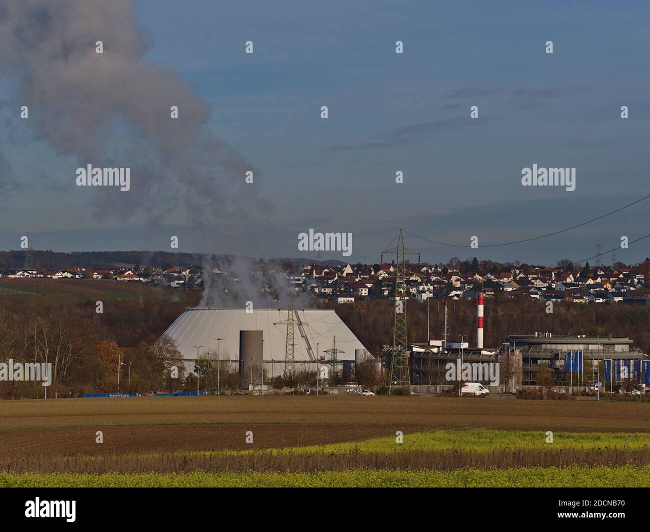Steaming cooling tower of nuclear power plant operated by utility company EnBW with agricultural fields in front and village Neckarwestheim. Stock Photo
