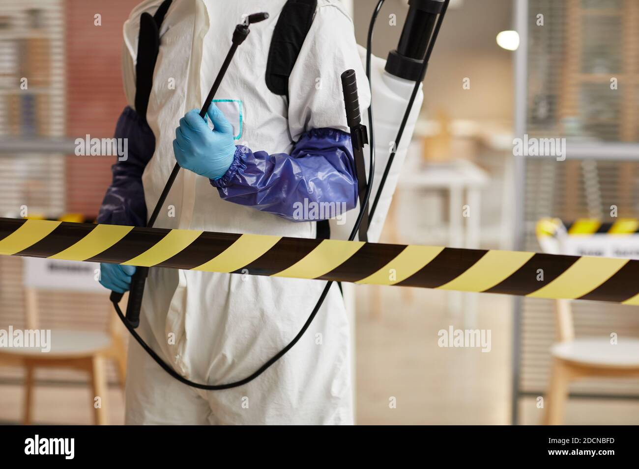 Cropped portrait of unrecognizable disinfection worker wearing full protective gear standing behind danger line while sanitizing office, copy space Stock Photo