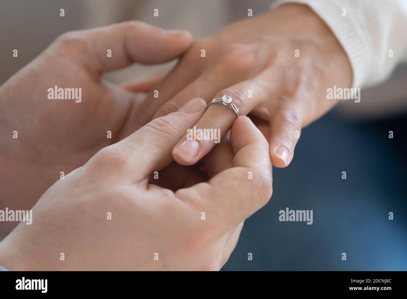 Happy groom putting engagement ring on finger of beloved bride Stock Photo