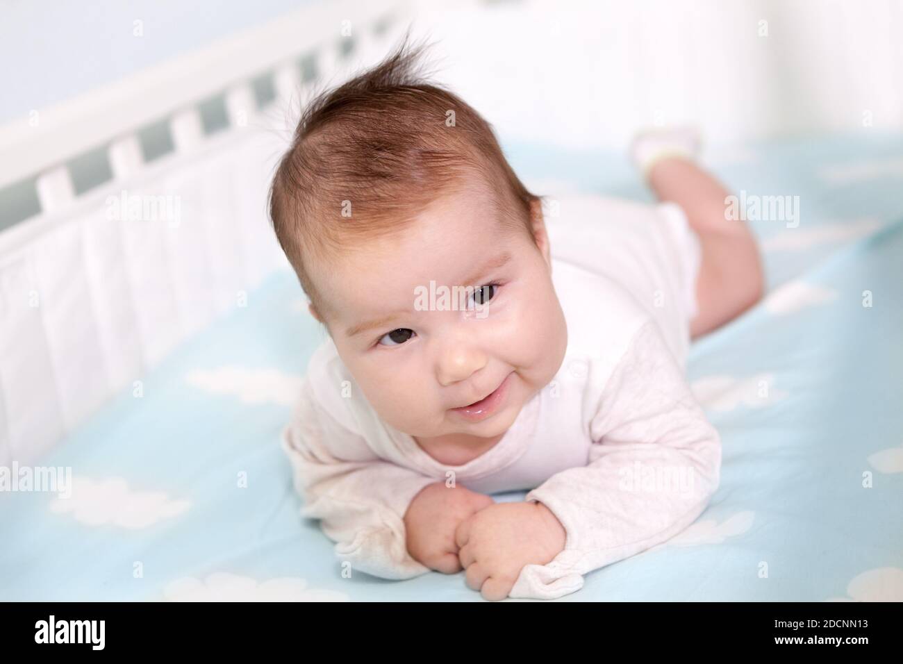 Sweet smiling newborn boy lying on his stomach in cot, trying to hold