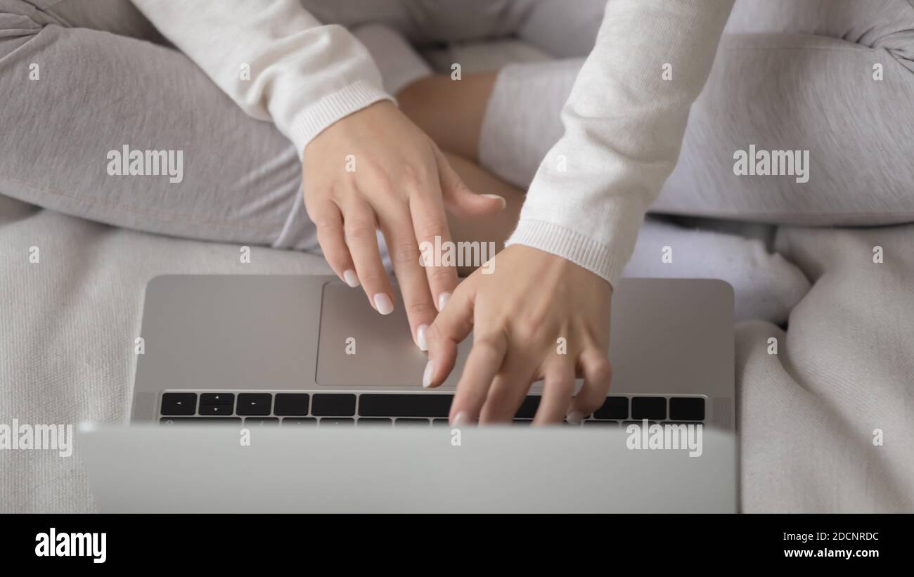 Busy young female freelancer sitting cross-legged on couch using laptop Stock Photo
