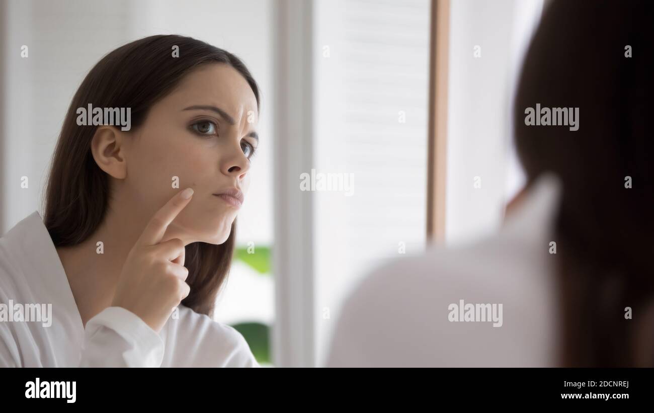 Stressed millennial female detecting acne on her cheeks Stock Photo