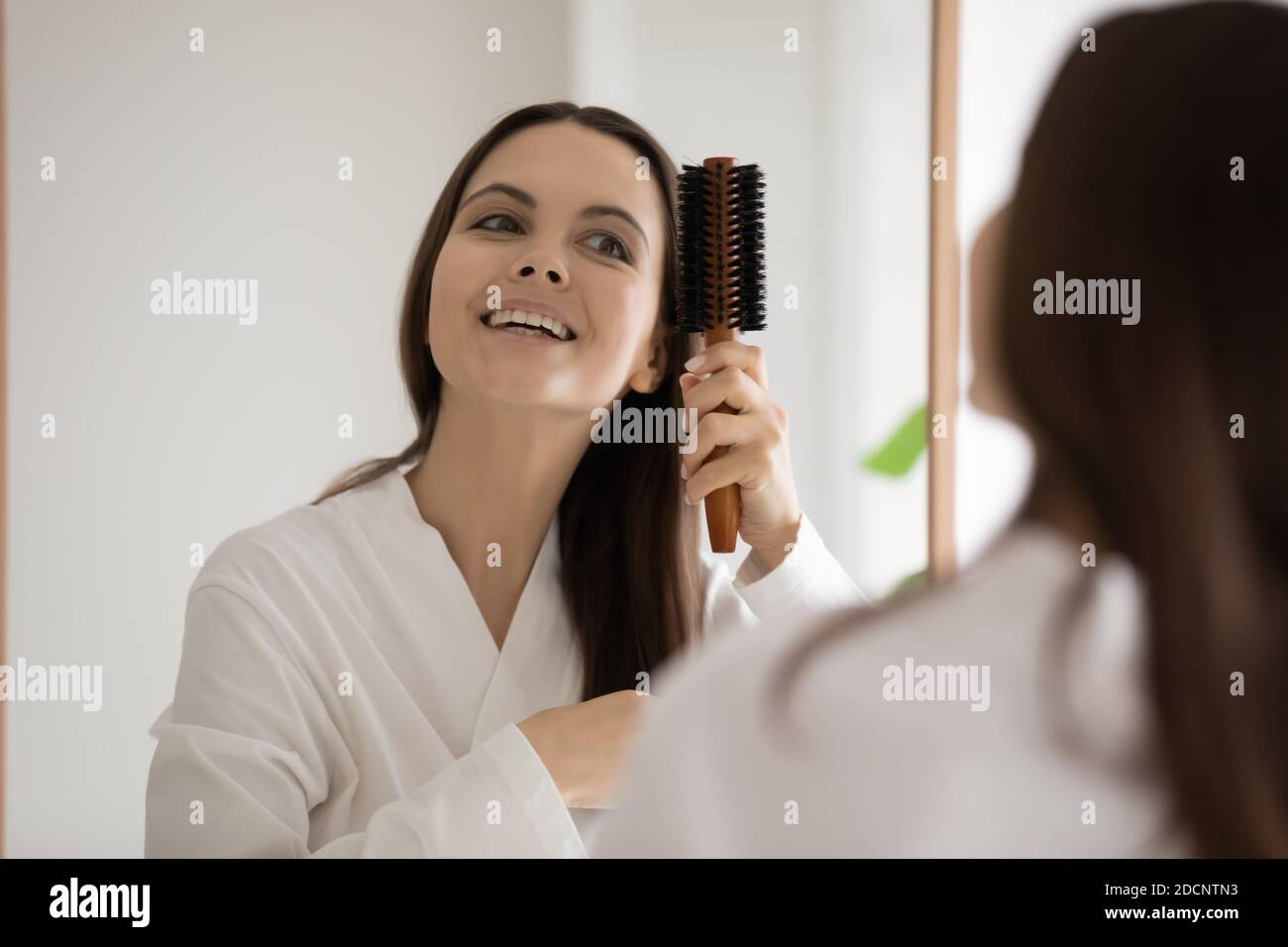 Happy young lady brushing hair after shower looking at mirror Stock Photo Alamy