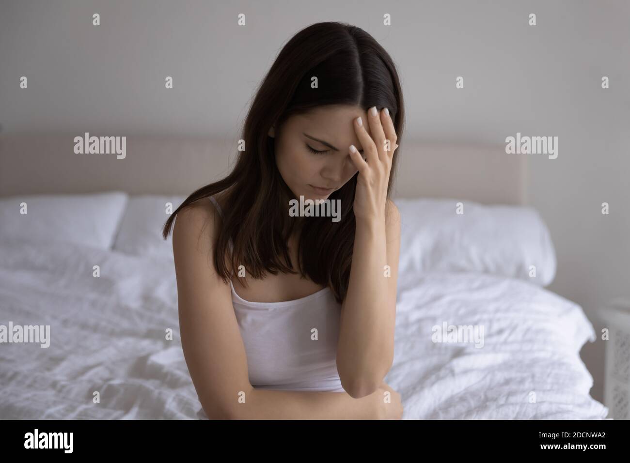 Frustrated young woman sitting on bed suffering from sudden headache Stock Photo