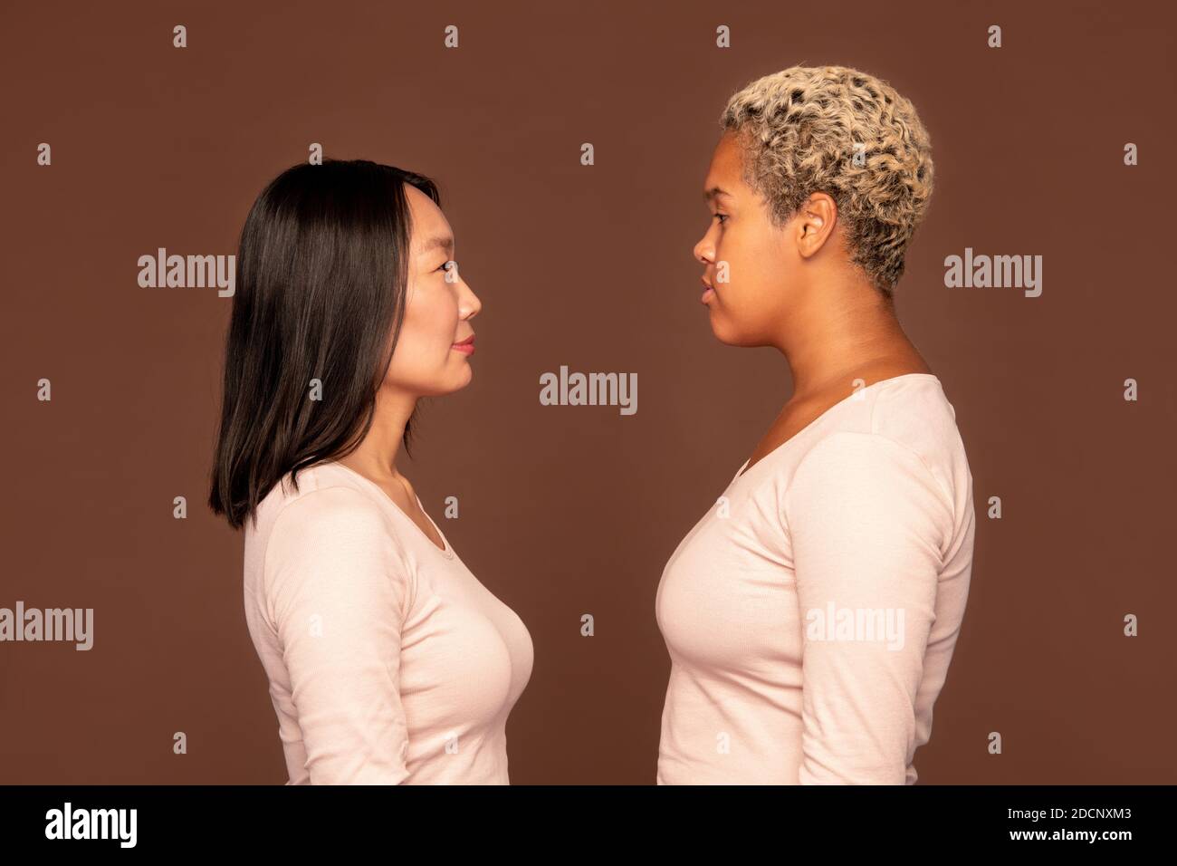Side view of two young intercultural women in white pullovers in front of camera Stock Photo