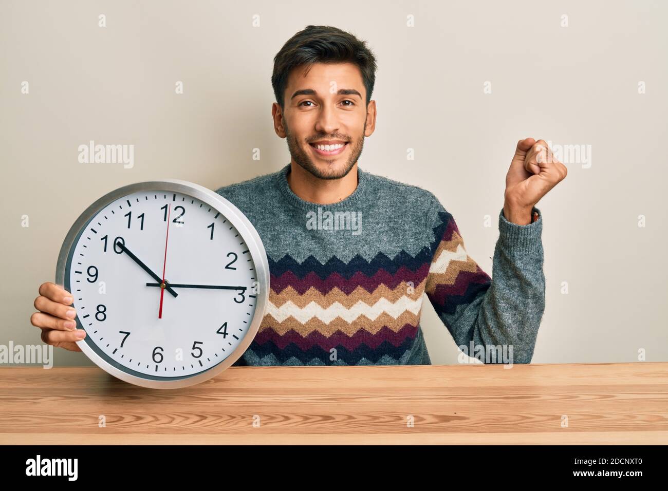 Young handsome man holding big clock screaming proud, celebrating ...