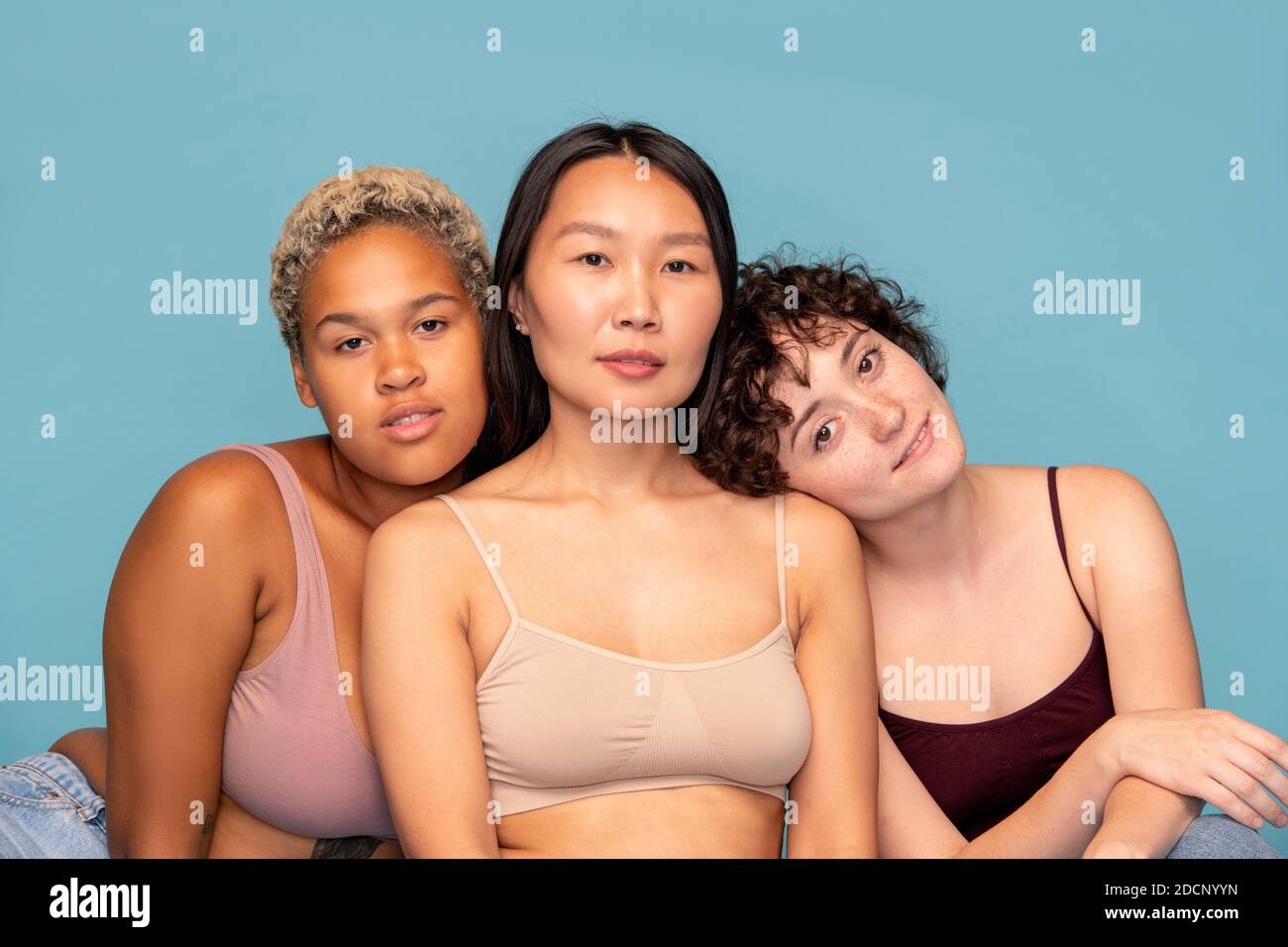Three affectionate and friendly girls in tanktops sitting close to one another Stock Photo