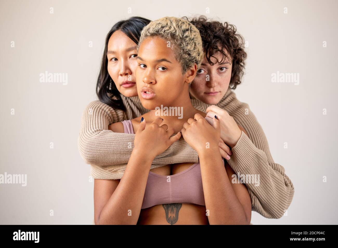 Women of Caucasian and Asian ethnicities in one sweater embracing African girl Stock Photo