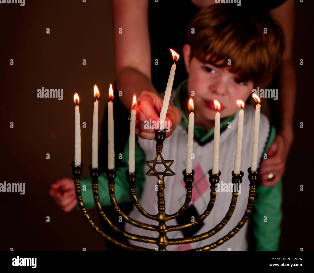 Young boy and his mother light the menorah candles during Chanukah