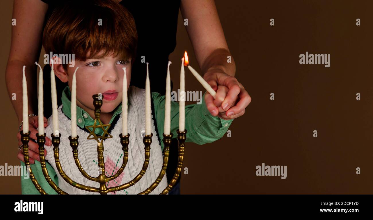 Young boy and his mother light the menorah candles during Chanukah