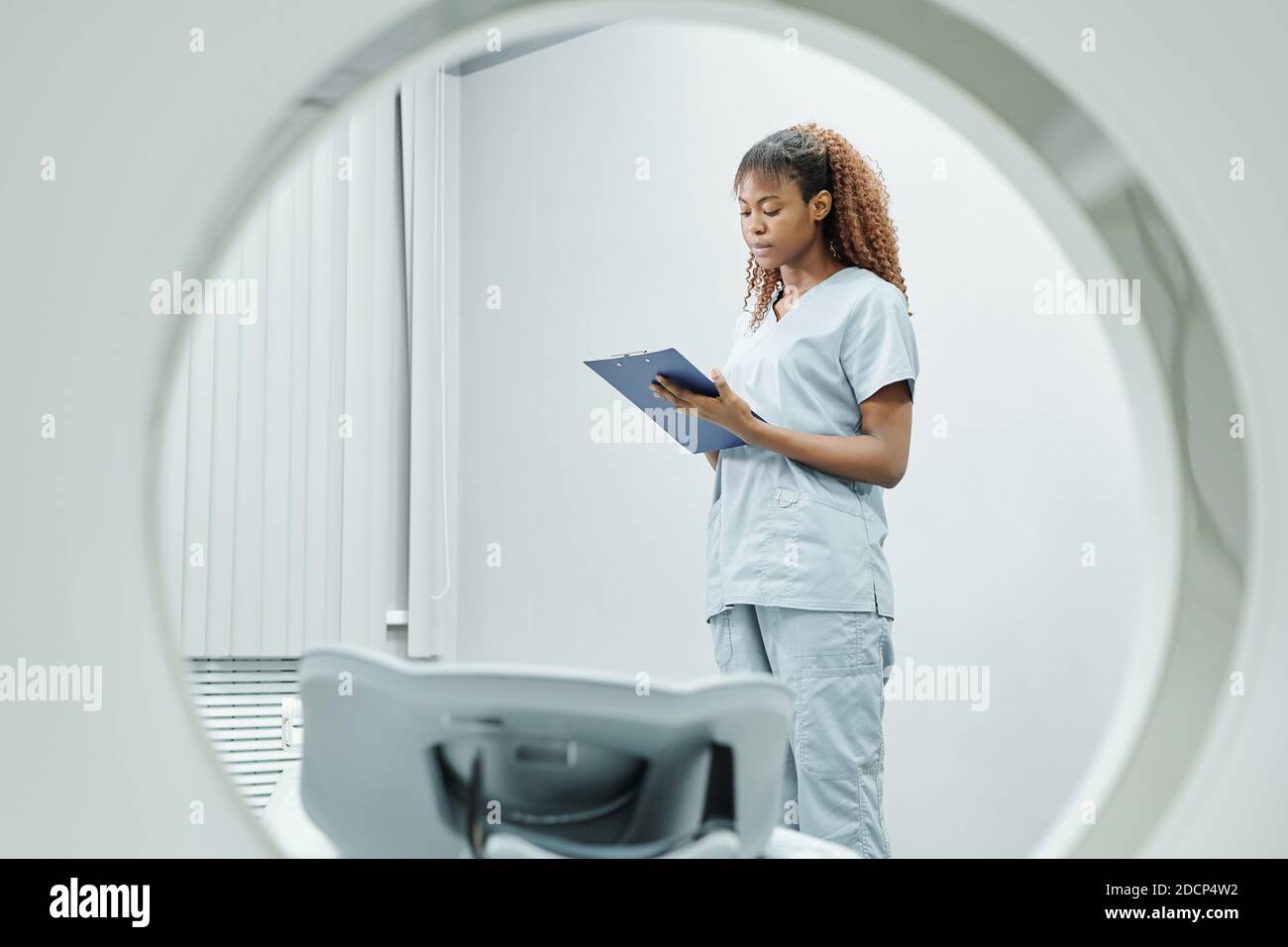 Young African nurse in uniform making notes in medical document by couchette Stock Photo