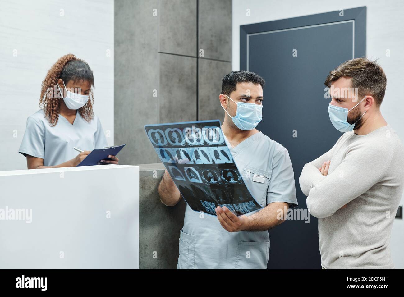 Serious male radiologist in uniform and mask showing x-ray image to ...