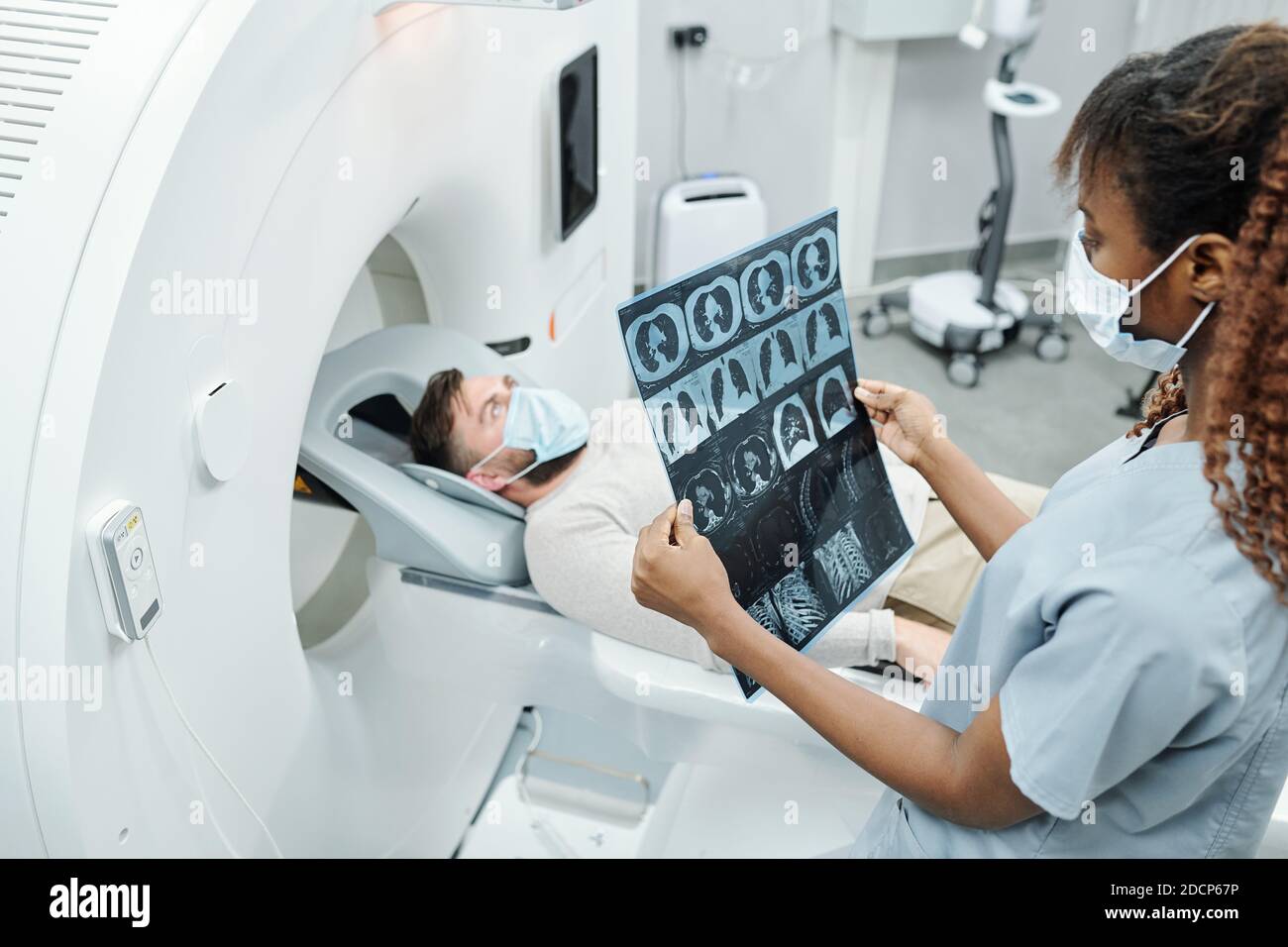 Young African radiologist in uniform and protective mask looking at x