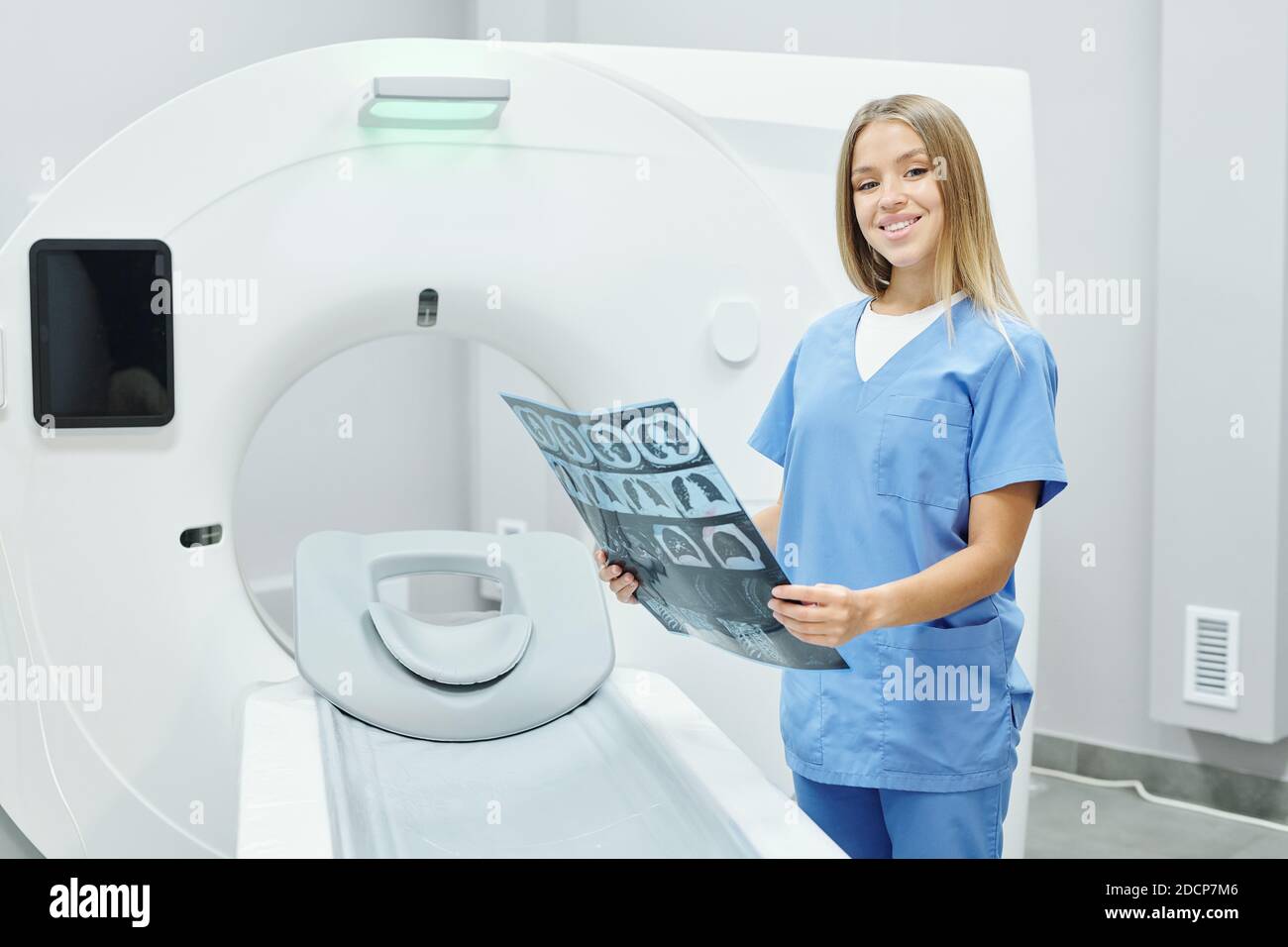 Happy young blond female radiologist in blue uniform analyzing x-ray image Stock Photo