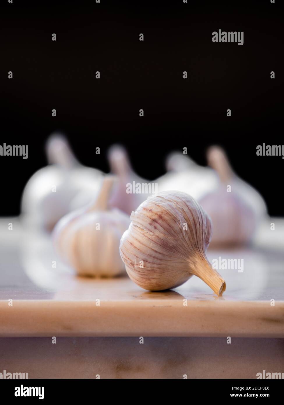 Garlic bulbs shot on a marble table top with emphasis on the front bulb. Stock Photo