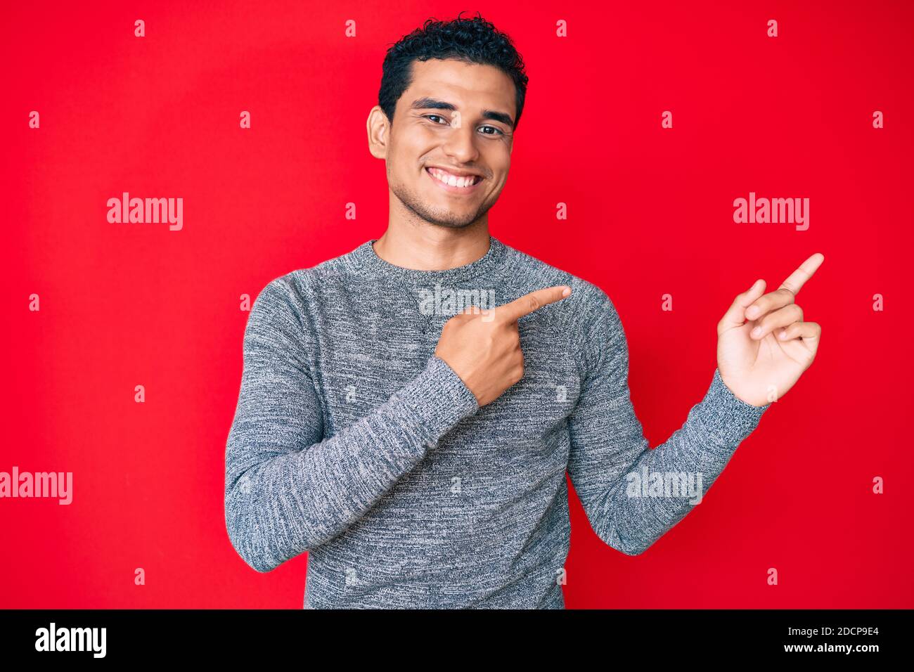Young handsome hispanic man over red background smiling and looking at ...