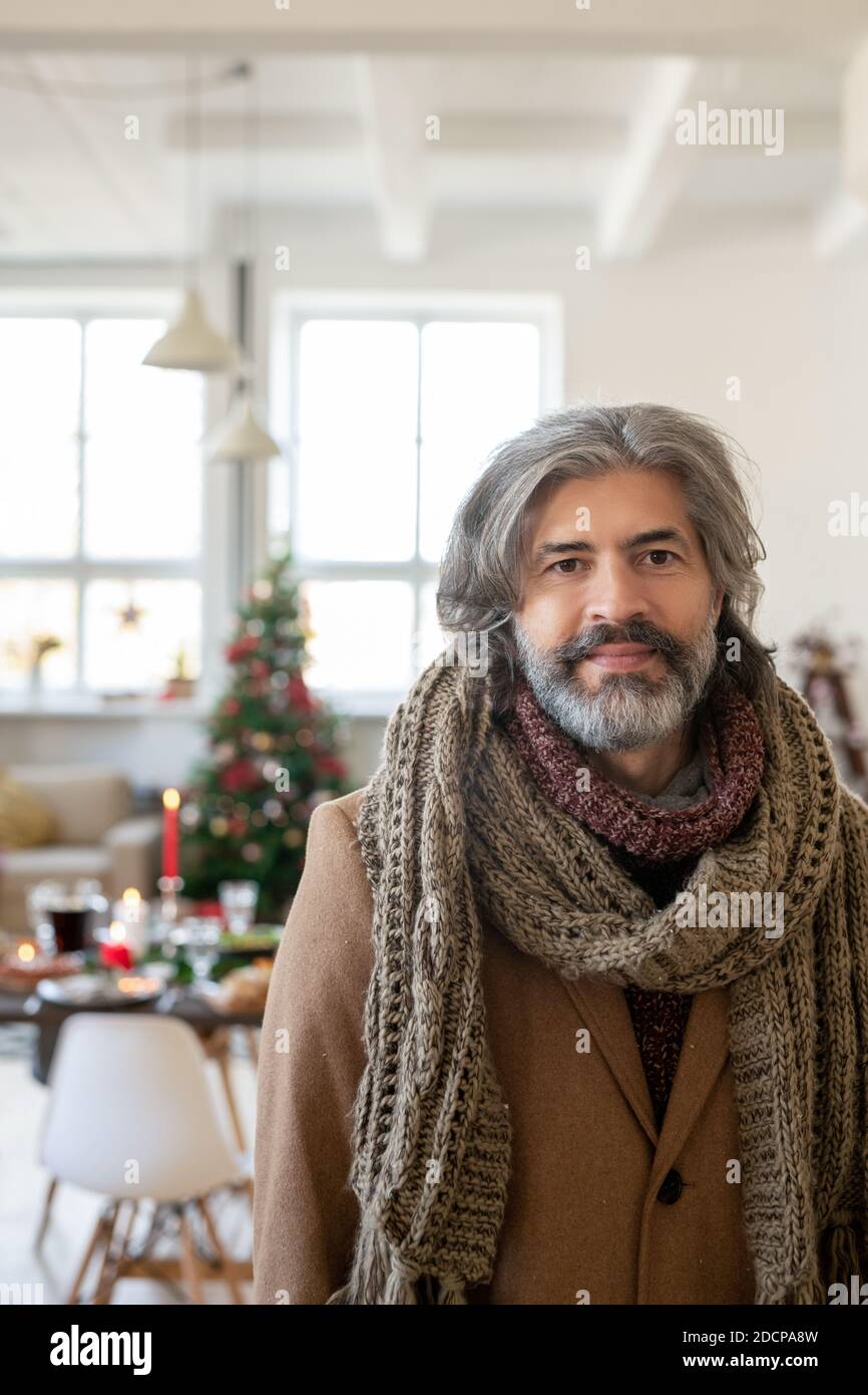 Mature greyhaired man in coat and knitted scarf standing in front of camera Stock Photo
