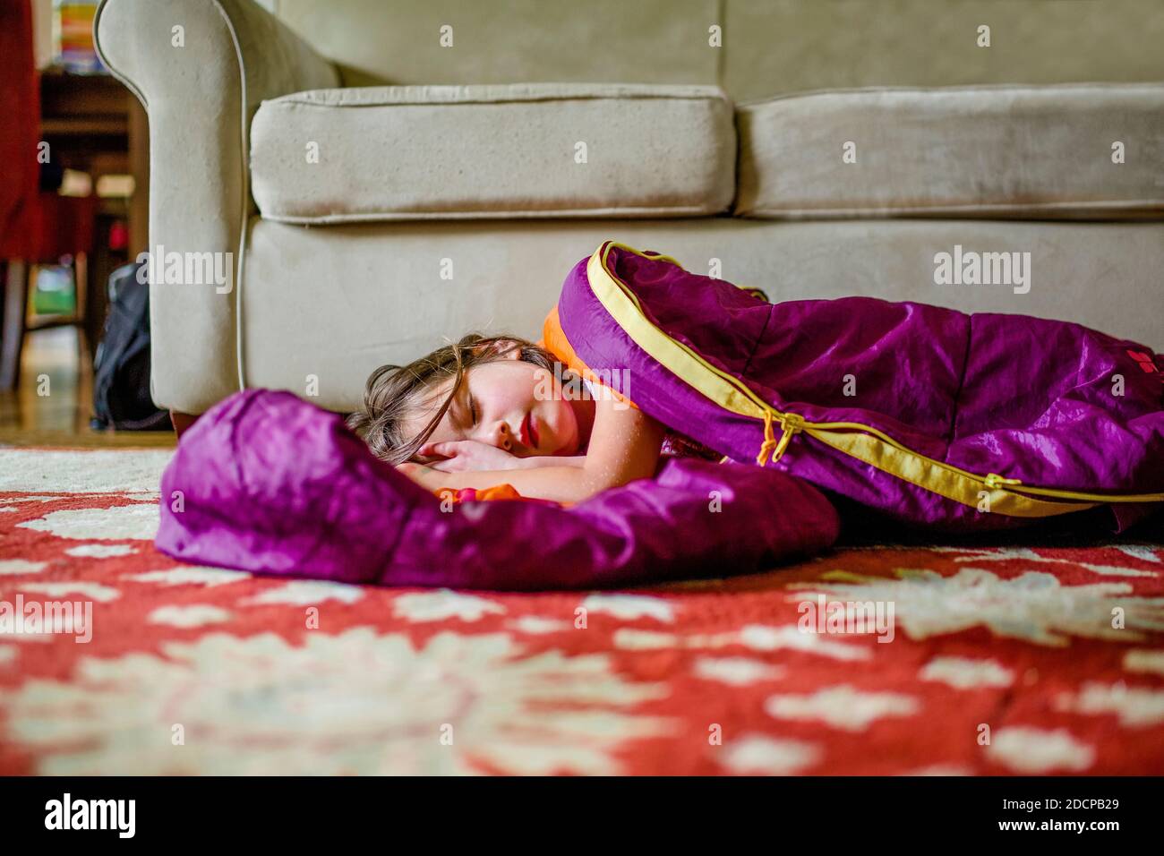 A beautiful little girl rests in a sleeping bag on the floor indoors