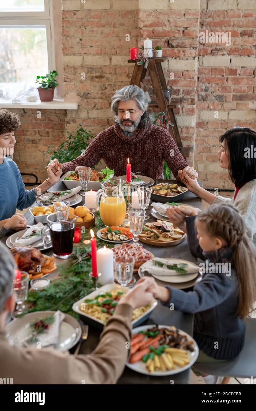 Large modern family of three generations praying by served festive table Stock Photo