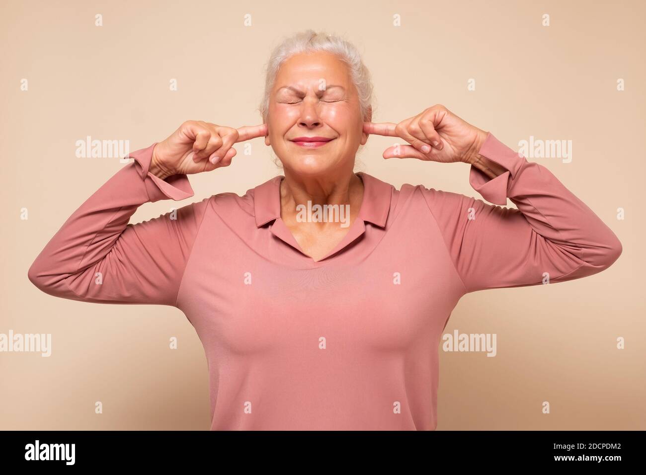 Angry annoyed senior woman plugging her ears to avoid loud noise Stock Photo