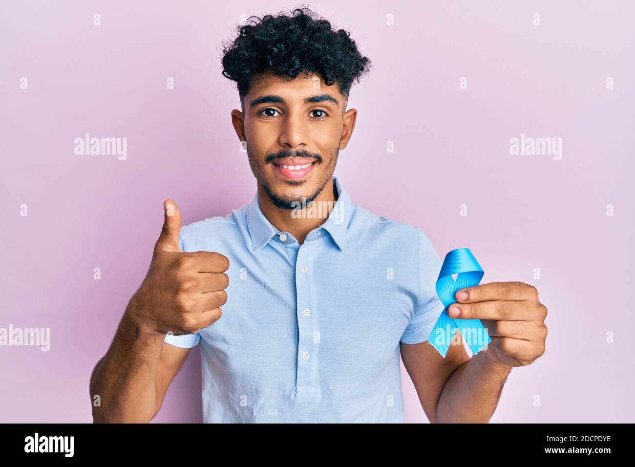 Young arab handsome man holding blue ribbon smiling happy and positive ...