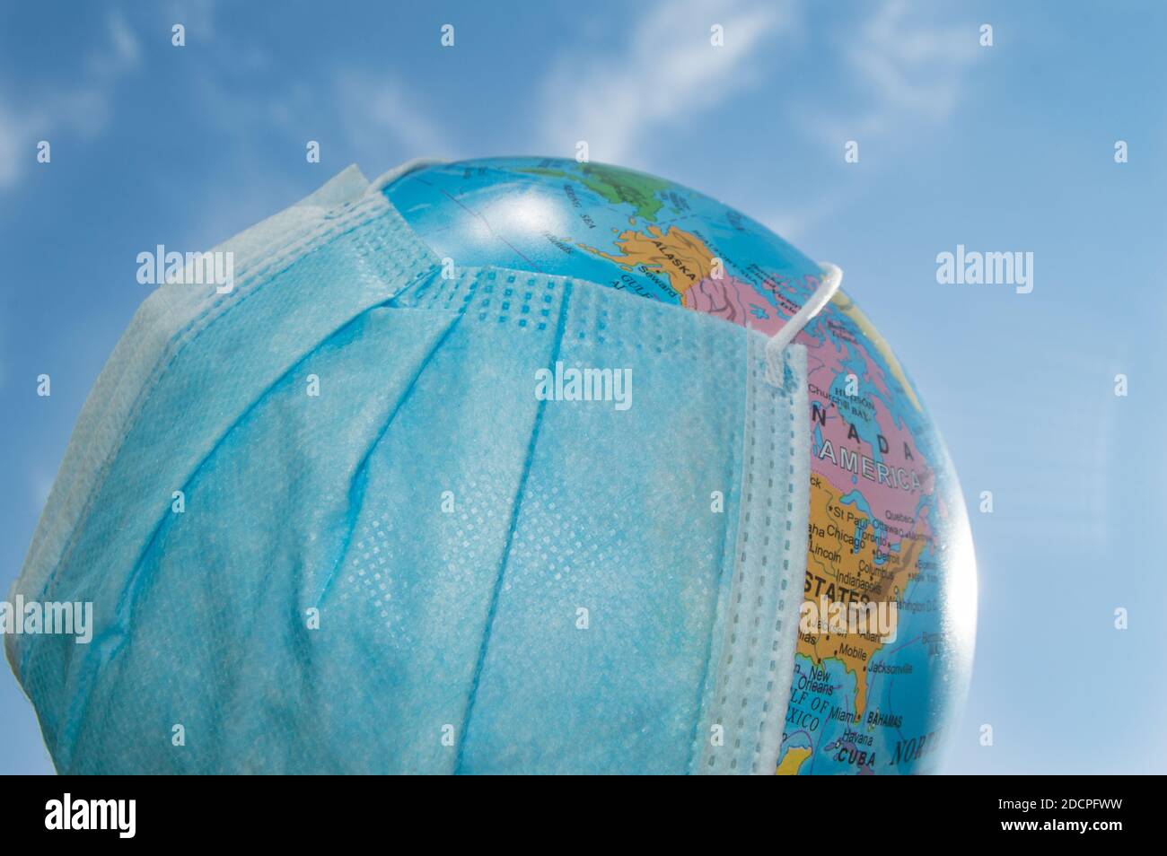 A globe in a medical mask against a blue sky. A worldwide pandemic, the concept of protection against coronavirus, outdoor, summer Stock Photo