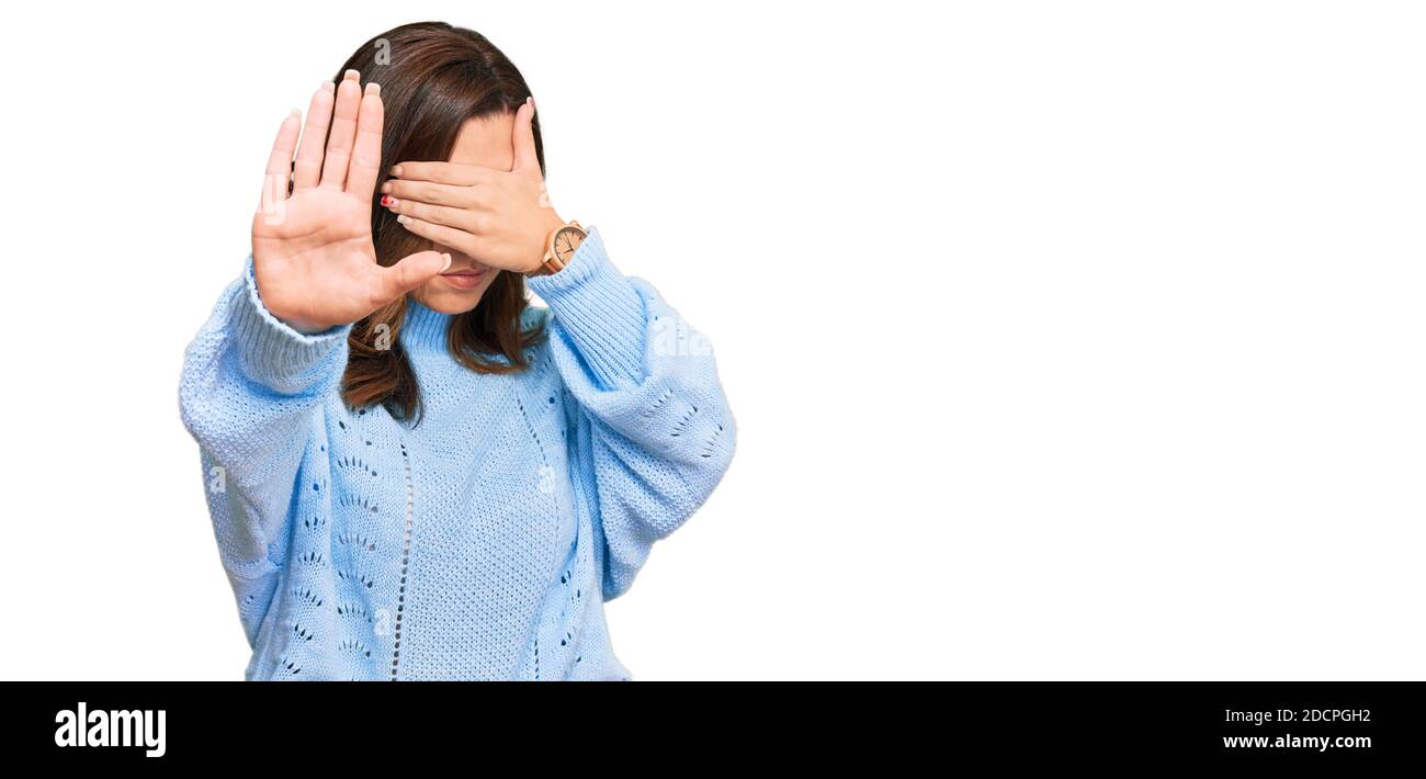 Young brunette woman wearing casual winter sweater covering eyes with hands and doing stop gesture with sad and fear expression. embarrassed and negat Stock Photo