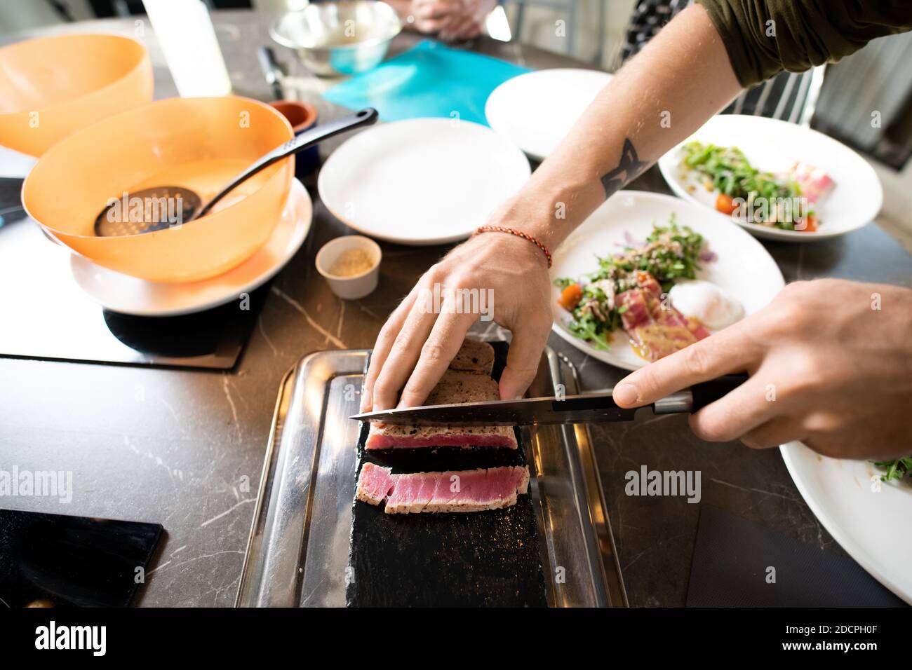 Hands of young male chopping piece of smoked or grilled beef on special board Stock Photo