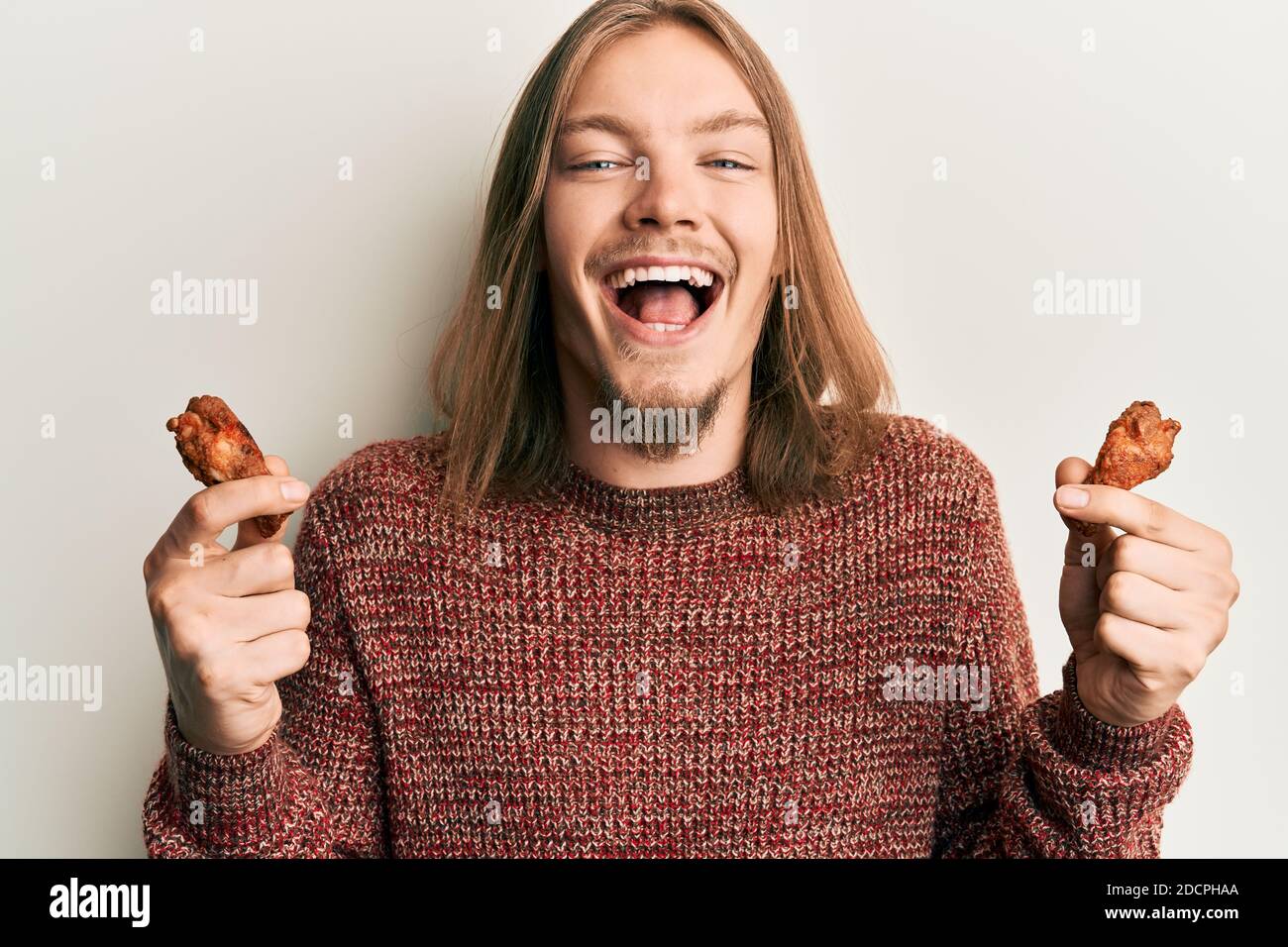 Handsome caucasian man with long hair eating chicken wings smiling and  laughing hard out loud because funny crazy joke Stock Photo - Alamy, image size:1300x956