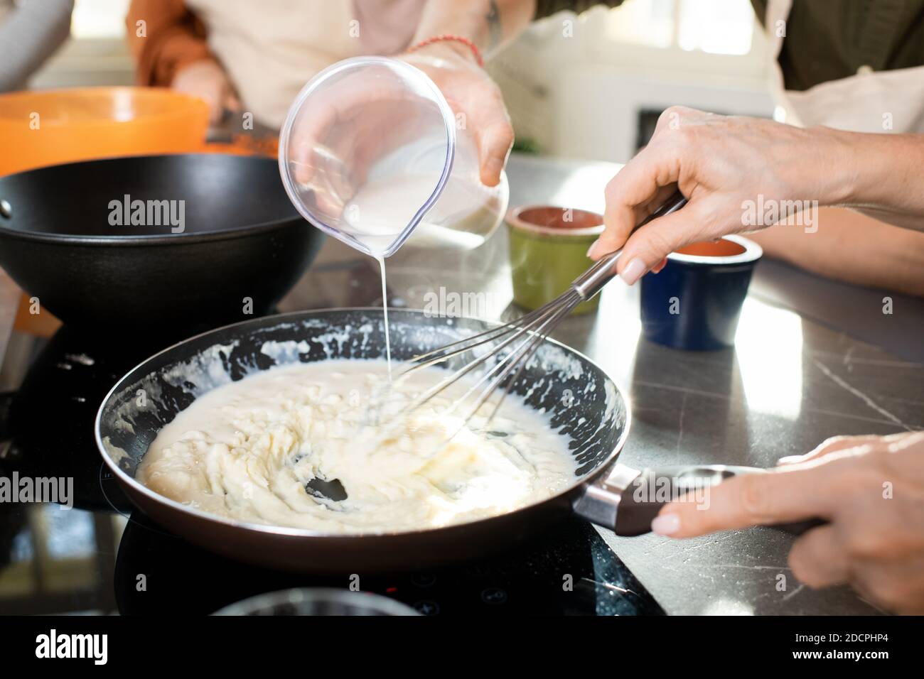 Hands of young man pouring milk into frying pan with flour while