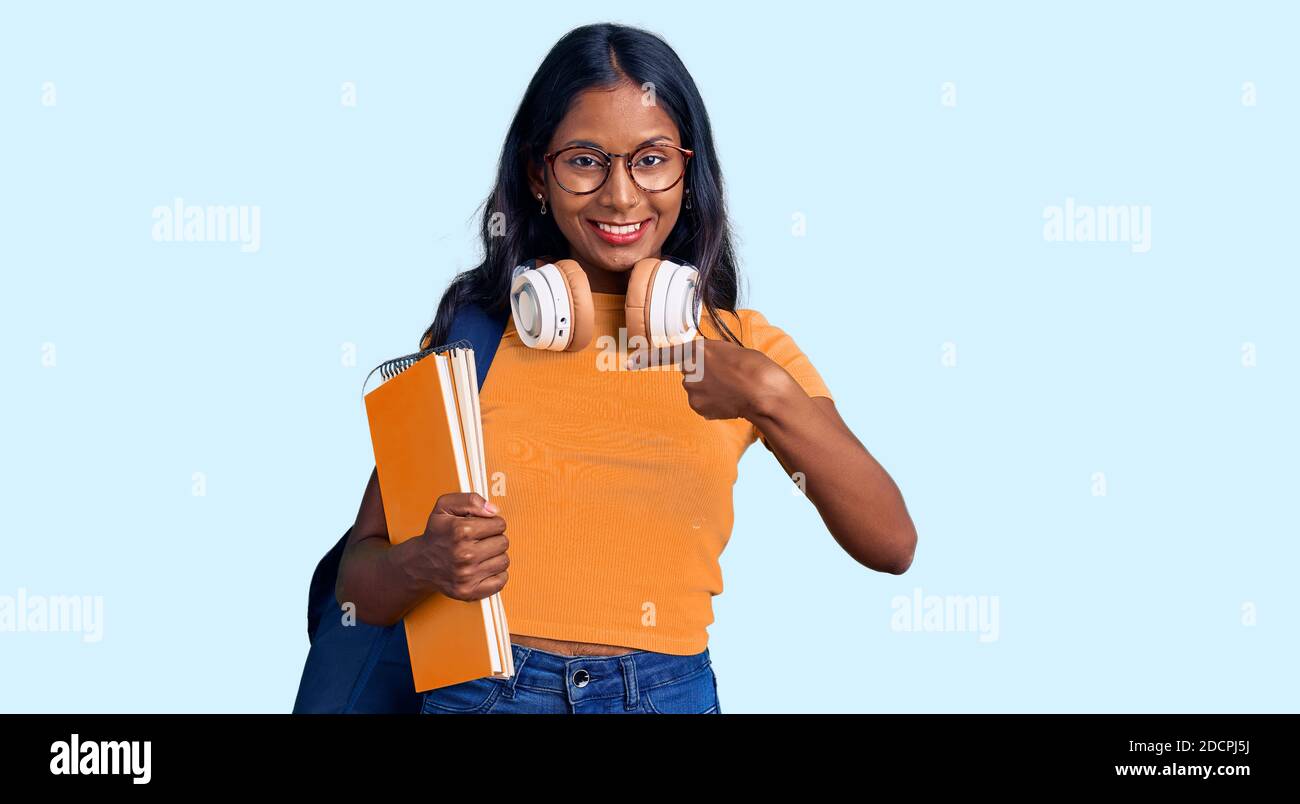Young indian girl holding student backpack and books pointing finger to ...