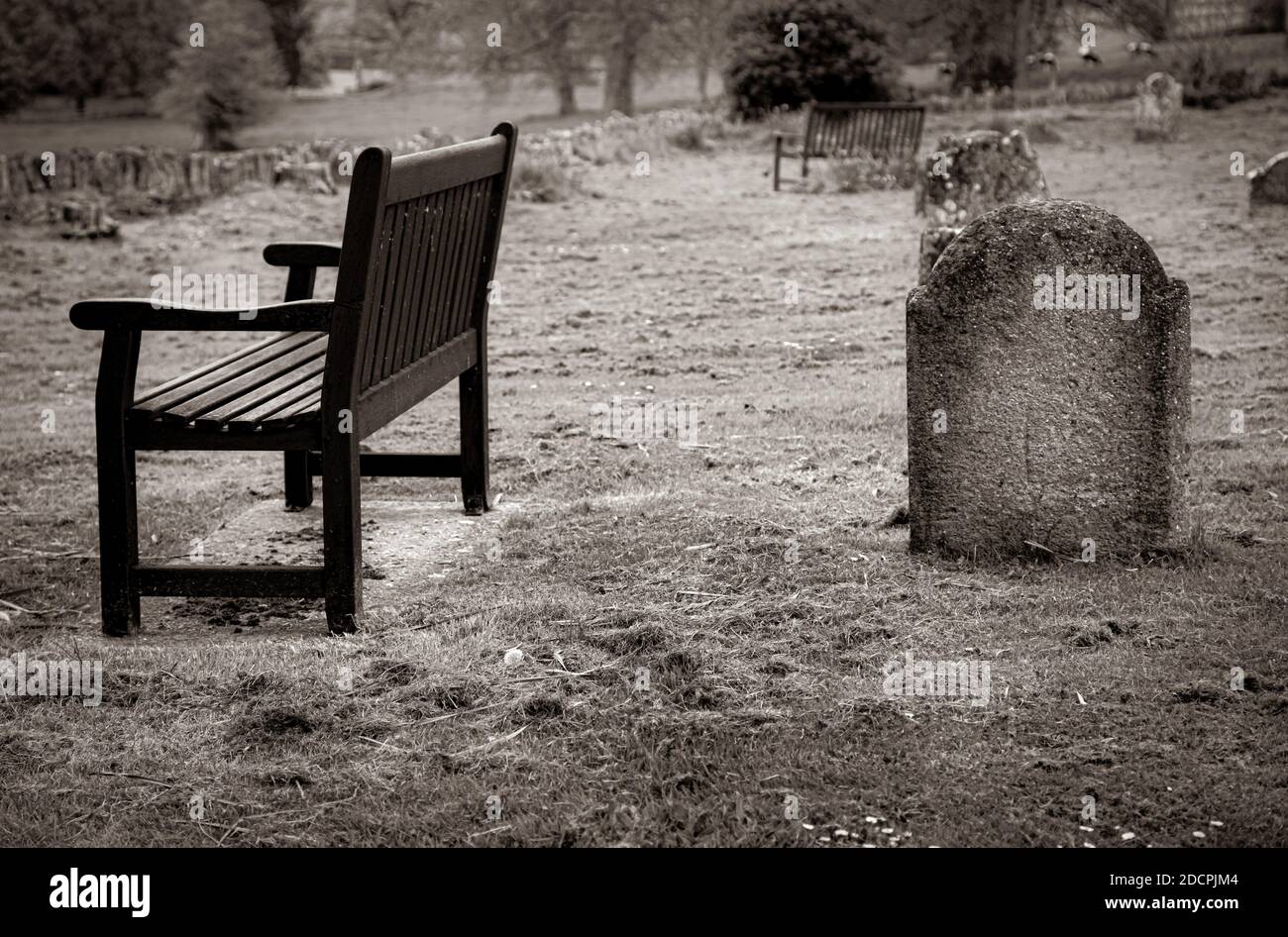 A lonely, peaceful scene of wooden benches in the parish graveyard alongside The St Michael & All Angels' church in Somerset,  East Coker, England, UK Stock Photo