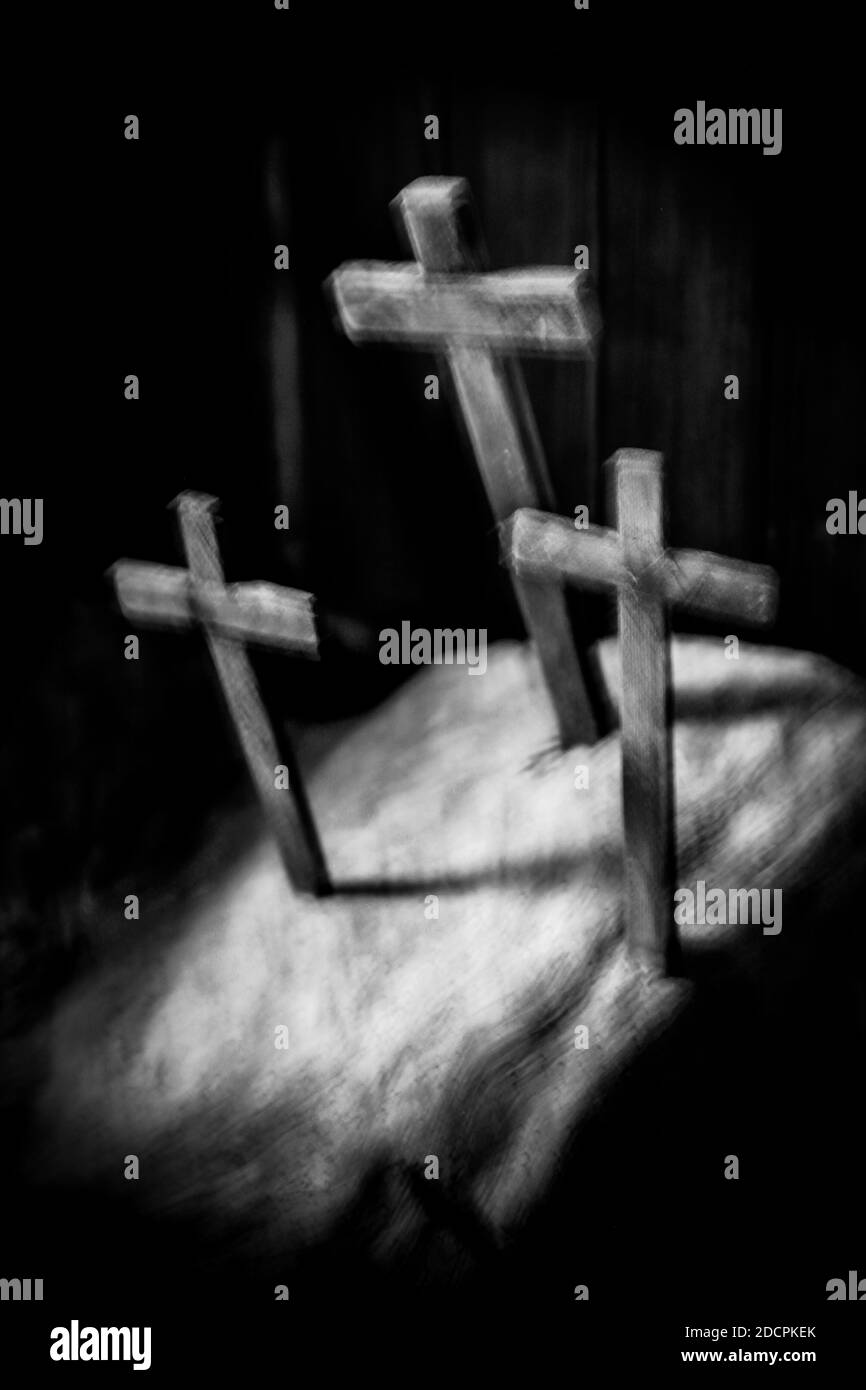 A blurry view of Three Wooden Crosses stabbed into a slab in a trinity pattern inside a dark  interior with light beaming down for spiritual concept Stock Photo