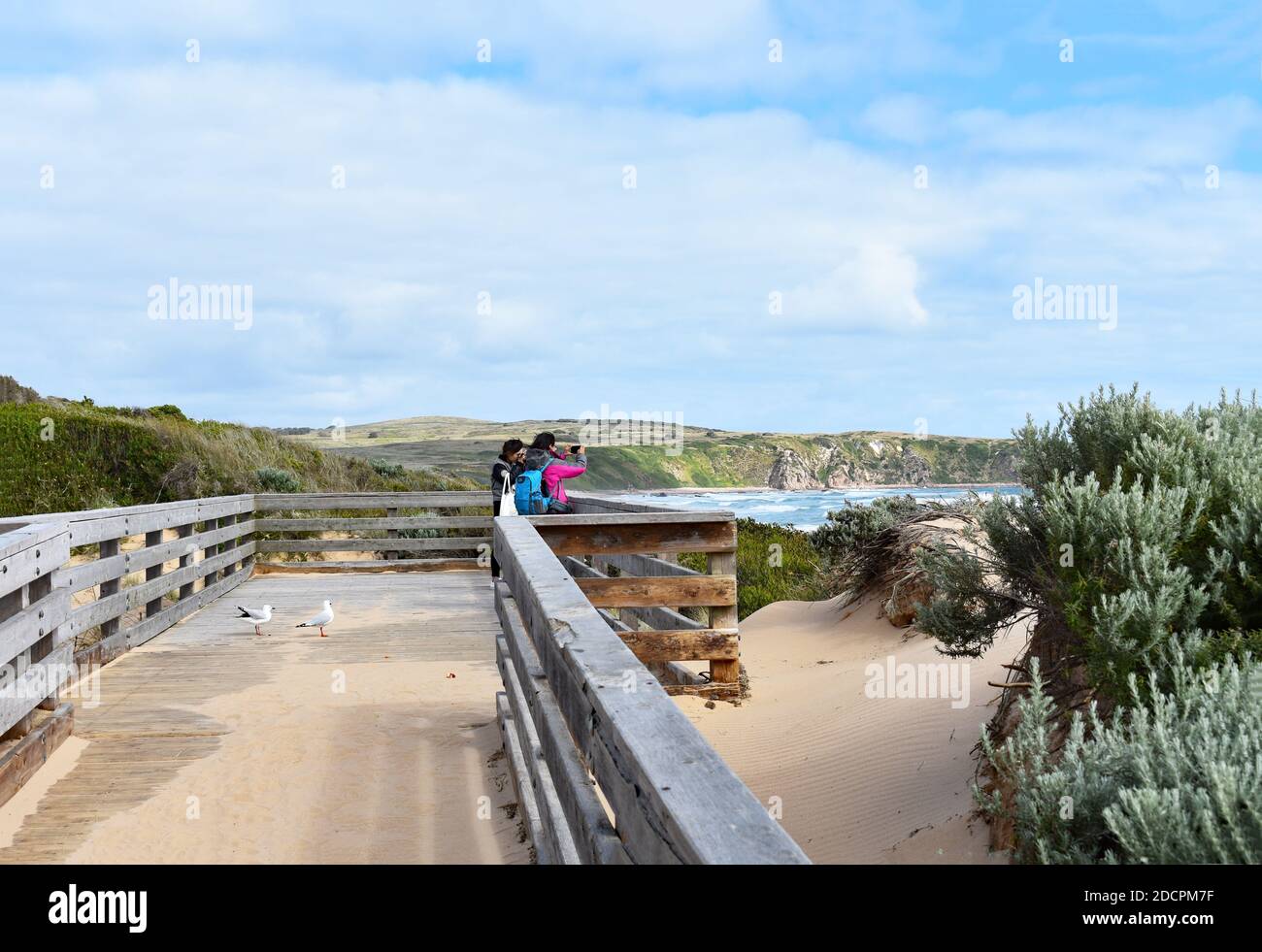 Two visitors taking photos stand on a wooden viewing platform overlooks Cape Woolamai Beach on Phillip Island, Victoria, Australia. Stock Photo
