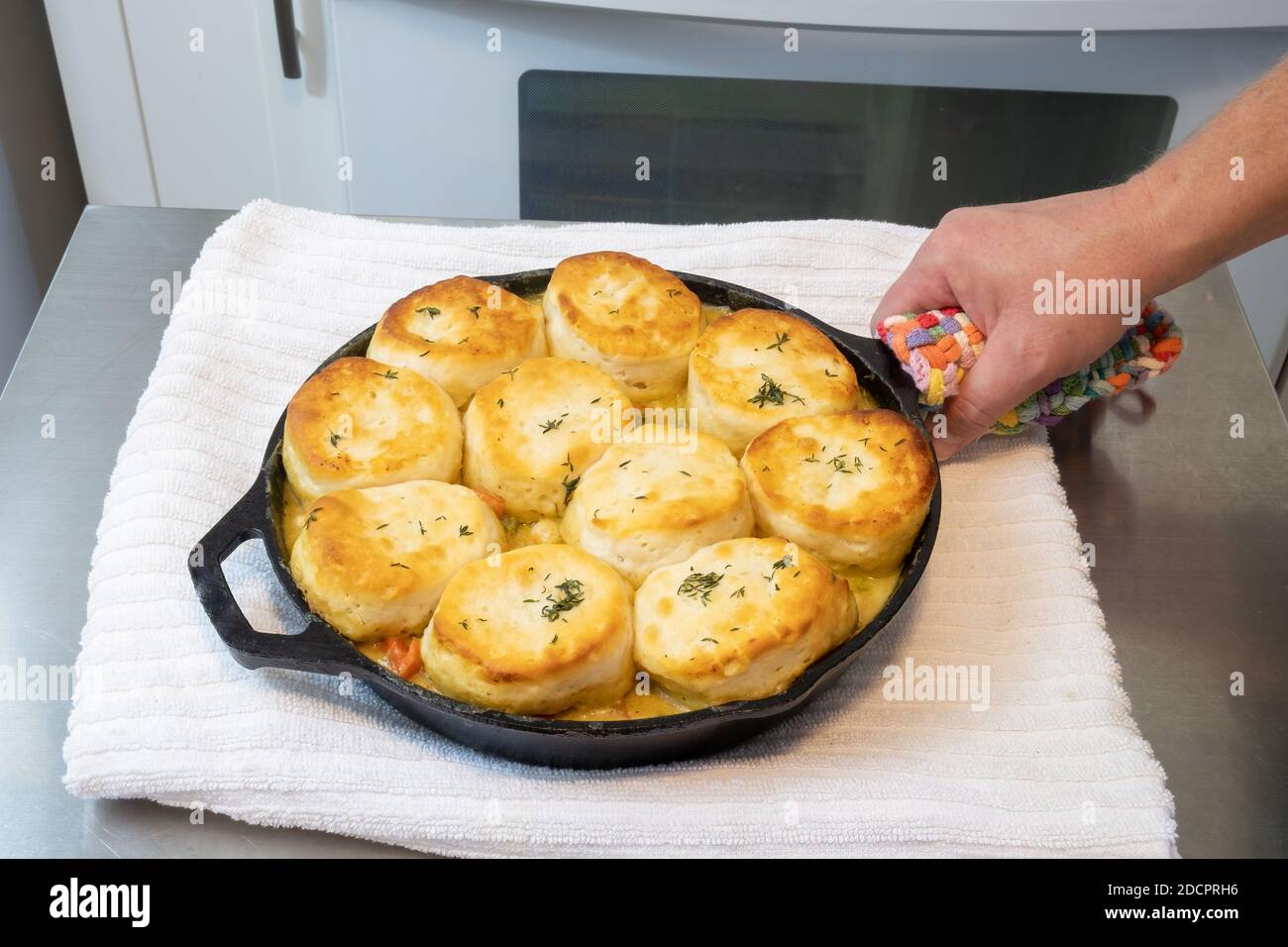 Chicken pot pie with biscuits used on top cooked to a toasty golden brown in a cast iron skillet with a man's hand holding it. Stock Photo