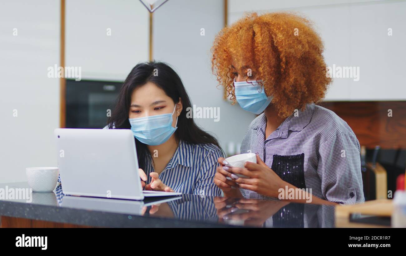 Two young women asian and black with face masks browsing social media on the laptop. High quality photo Stock Photo