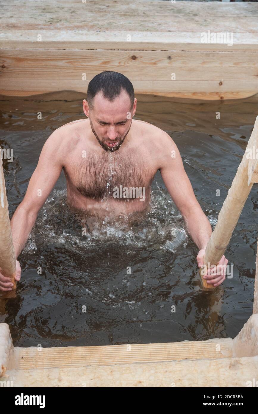 Nizhny Tagil, Russia - January 19, 2020: Man bathes into cold water of ice-hole on Epiphany day. Traditional ice swimming in Orthodox church Holy Epip Stock Photo